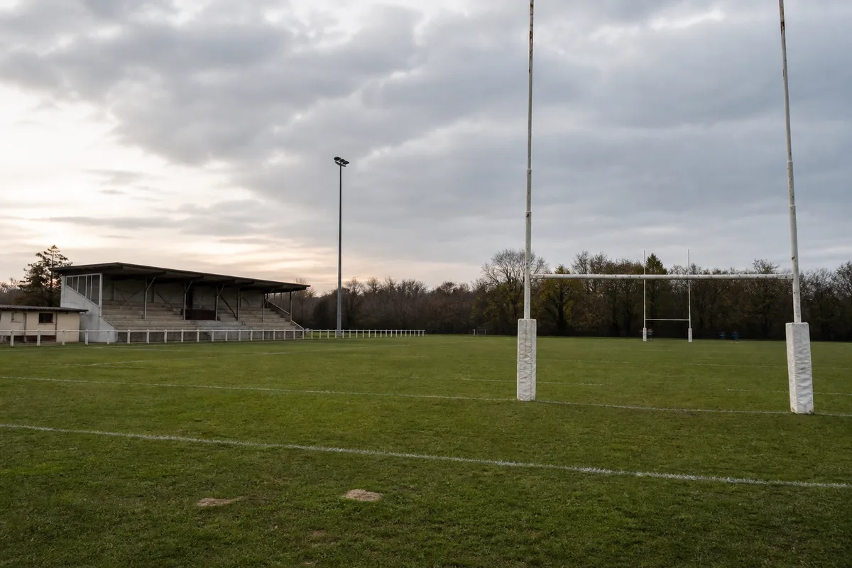 Terrain de rugby de club amateur avec ses poteaux et sa tribune modeste, en fin de journée