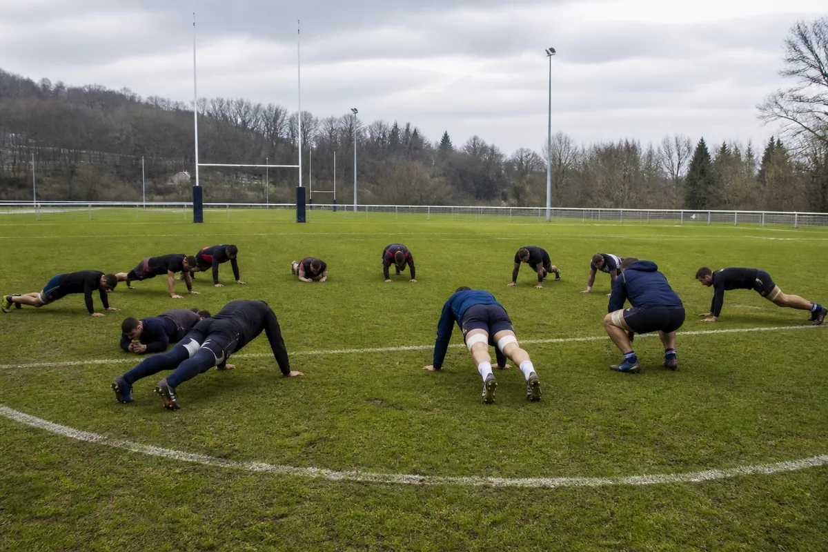 Groupe de joueurs de rugby en séance de renforcement sur un terrain, exercices au poids de corps en cercle